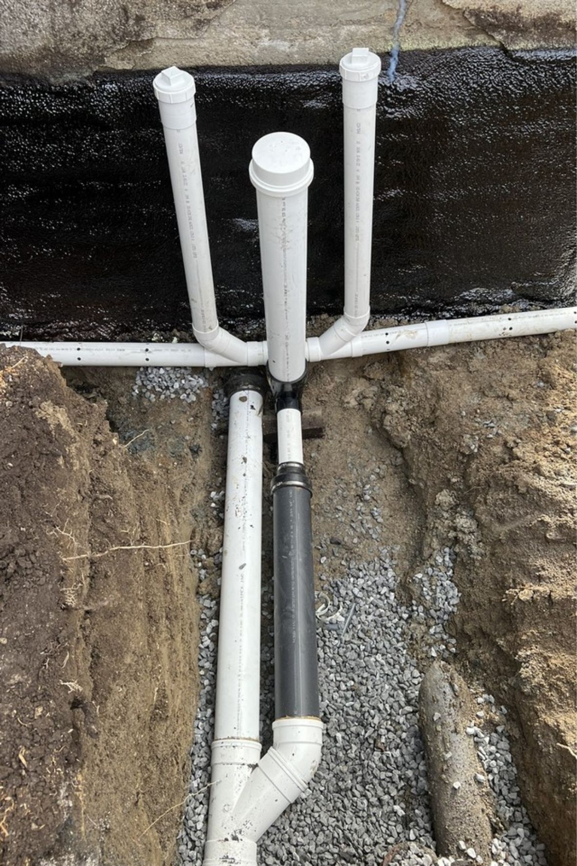 Tuyaux installés le long d’un mur de fondation avec revêtement noir et gravier sur la Rive-Sud de Montréal